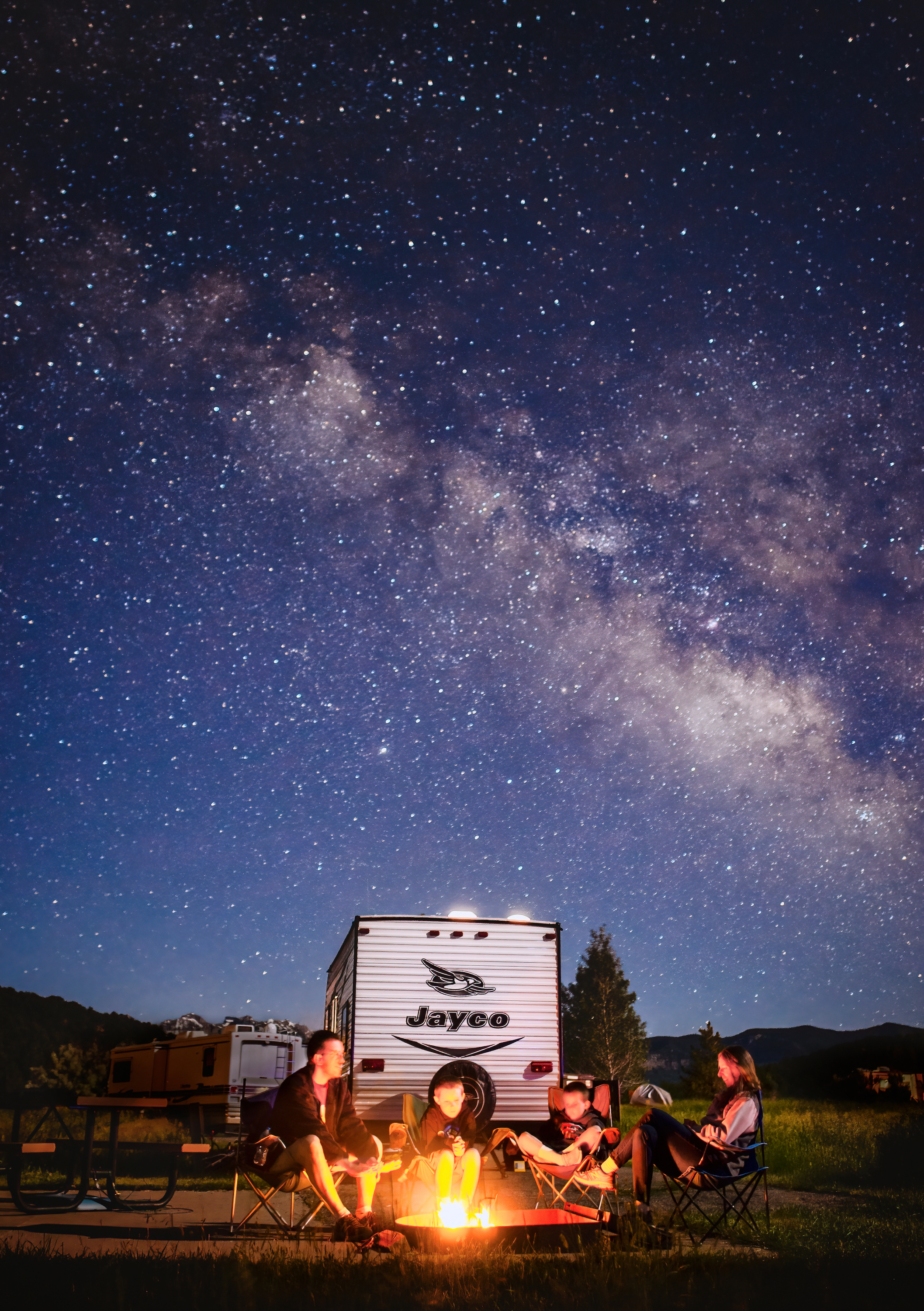 Alison Takacs's family around a campfire with their Jayco travel trailer and a starry sky in the background.