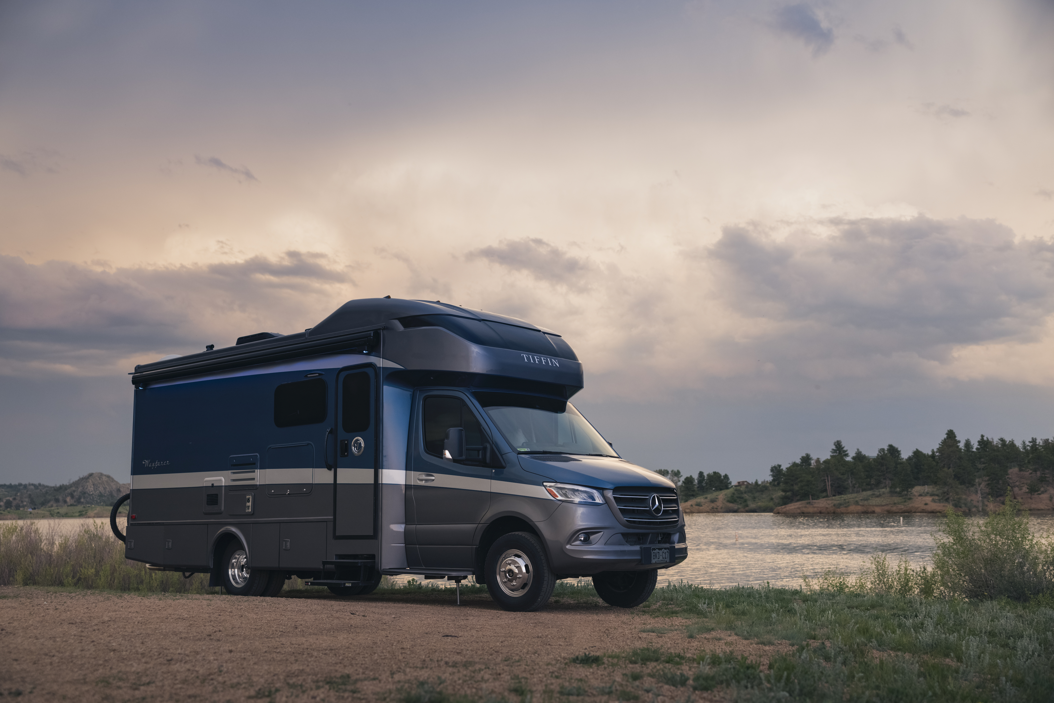 Dustin and Sarah's Tiffin Wayfarer parked at a campsite near a lake.