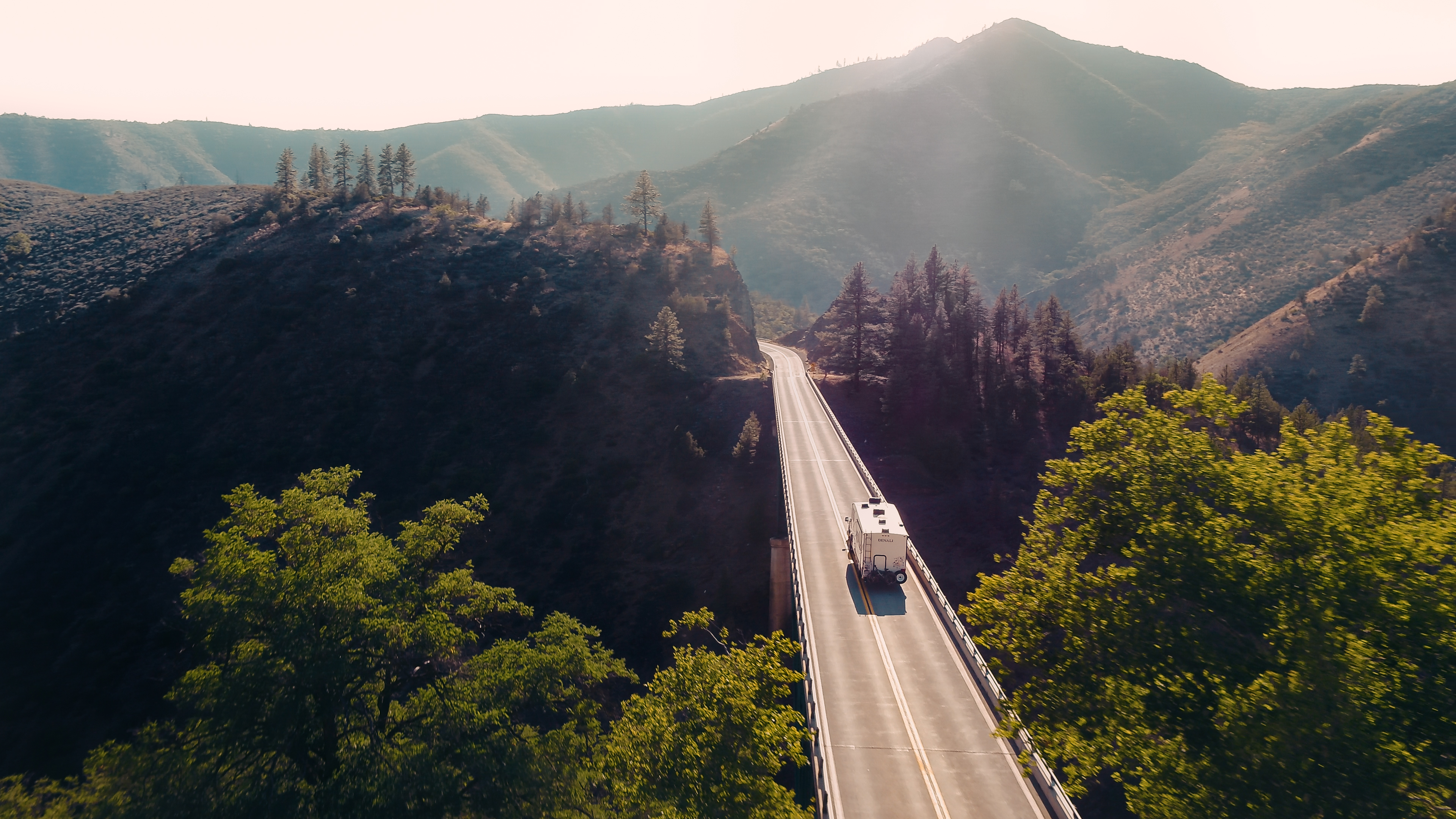 A fifth wheel RV driving down a bridge through mountains. 