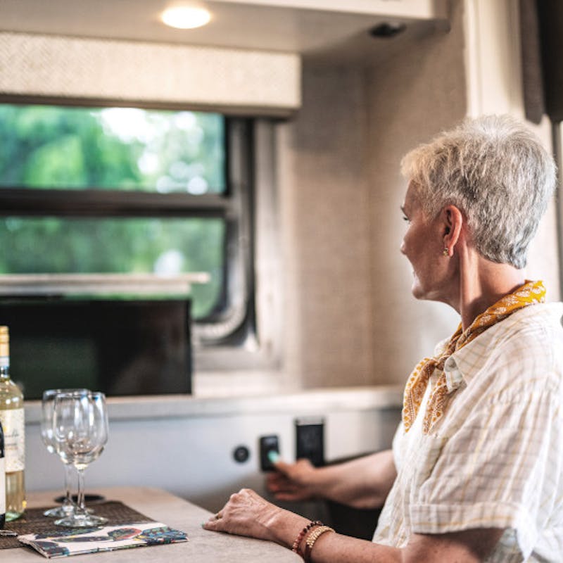 A woman flips a switch to mount the television next to a dinette with wine glasses in a Jayco Entegra Vision RV.