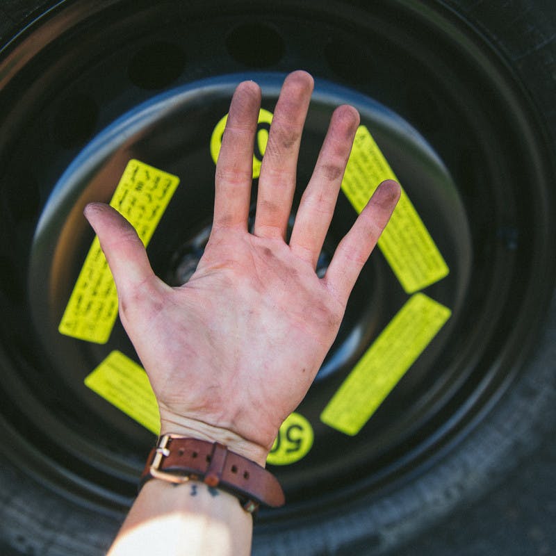 A dirty hand in front of a spare tire after changing a flat on the side of the road.
