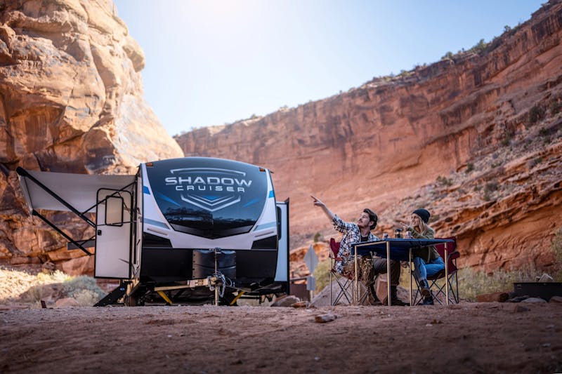 A man and a woman pointing at rocky landscape next to a shadow cruiser rv