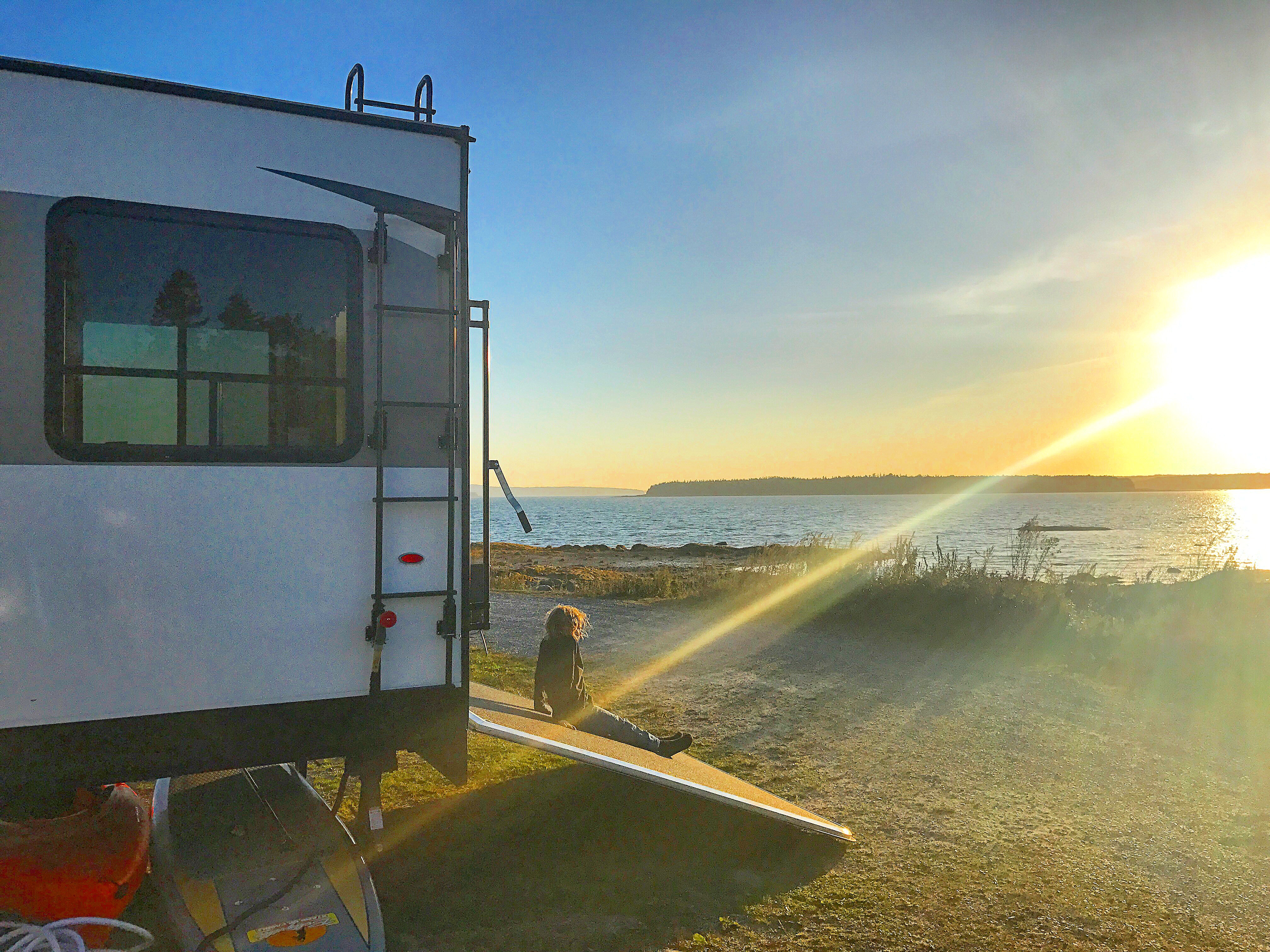 A little boy sitting on the back ramp of a Toy Hauler, watching the sun set. 