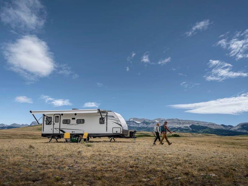 A couple hiking away from a keystone passport travel trailer