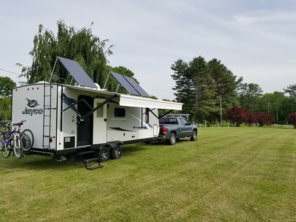 CHRISTINA AND BEN MCMILLAN's RV parked in a field with solar panels attached to the roof of the RV