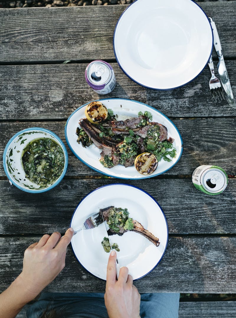 A serving of lamb plated and being cut into by two hands holding a fork and knife.