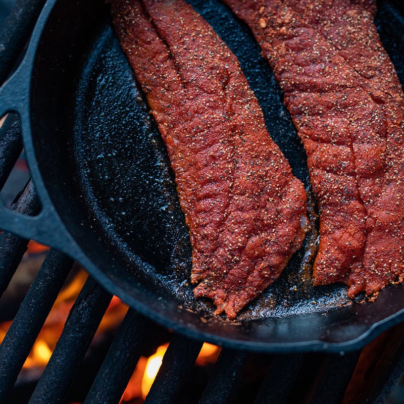 Filets being grilled in a pan over a fire.